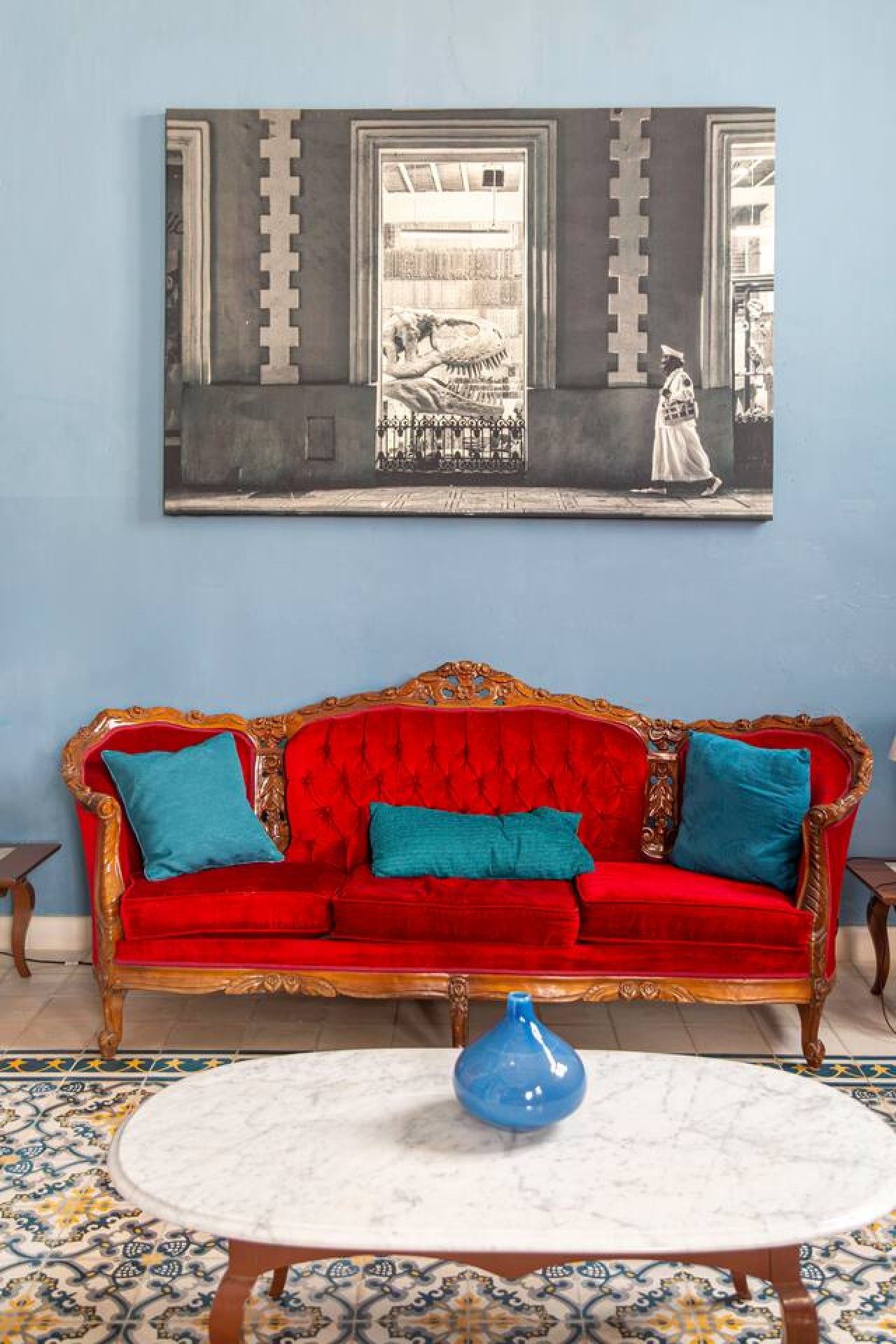 Una habitación con un sofá de terciopelo rojo, un jarrón azul y un cuadro grande en la pared.