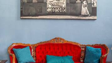 Una habitación con un sofá de terciopelo rojo, un jarrón azul y un cuadro grande en la pared.