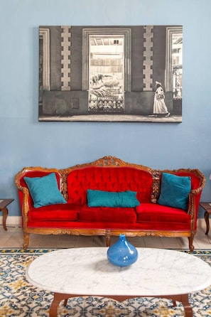 Una habitación con un sofá de terciopelo rojo, un jarrón azul y un cuadro grande en la pared.