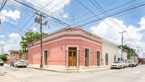 Um edifício de dois andares com telhado plano e fachada vermelha. Vários veículos estão estacionados na rua em frente.