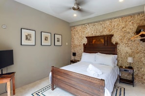 Un dormitorio con cama de madera, televisor, cuadros enmarcados en la pared y pared de piedra.
