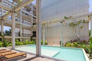 Uma área de piscina ao ar livre com vários níveis, estrutura em concreto, rodeada por vegetação e espreguiçadeiras de madeira.