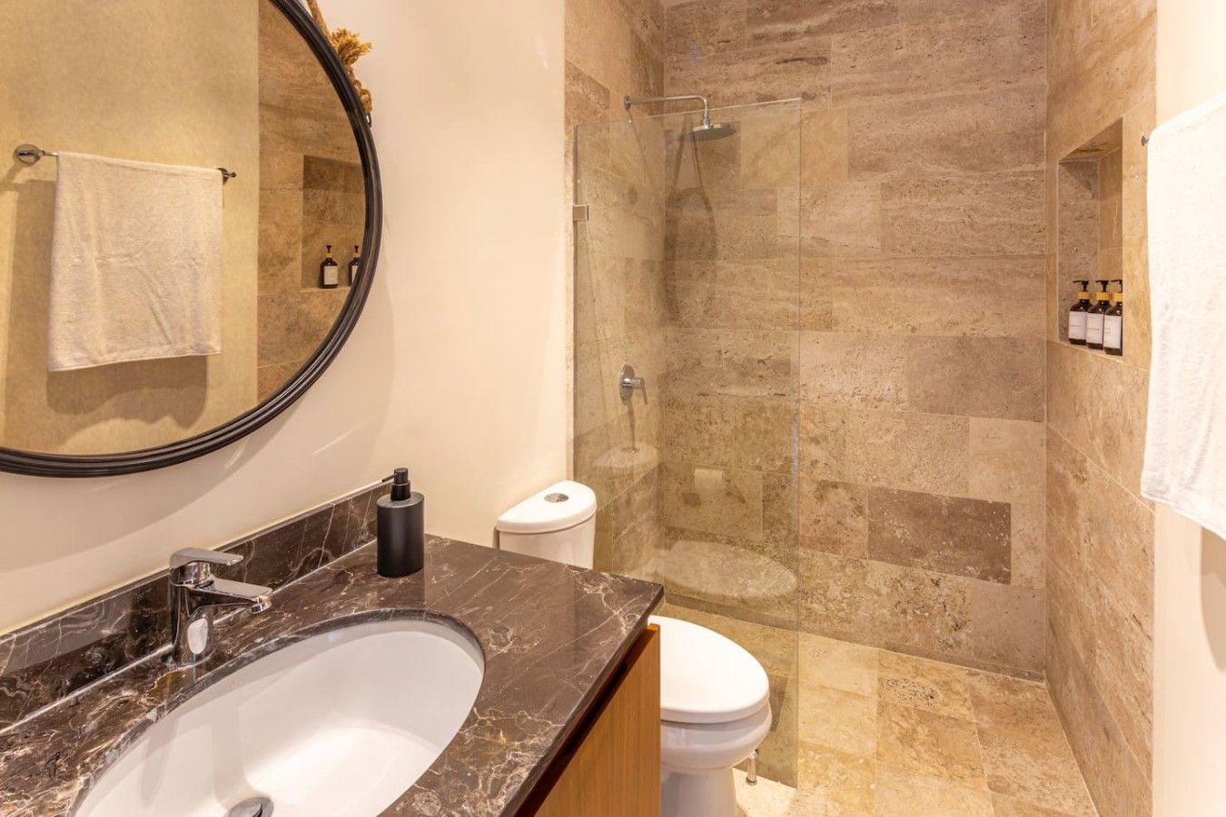 Une salle de bain avec un lavabo en marbre, des toilettes, une douche à parois de verre et un miroir.