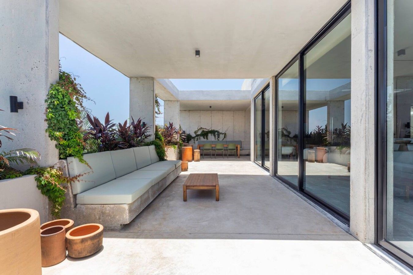 Un patio moderno al aire libre con un sofá, una mesa de madera y plantas en macetas.