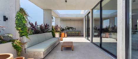 Un patio moderno al aire libre con un sofá, una mesa de madera y plantas en macetas.