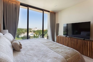 Quarto de hotel moderno com uma cama grande, televisão de tela plana e varanda com vista para a cidade.