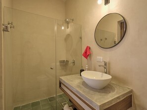 Ein Badezimmer mit einer gläsernen Dusche, einem weißen Waschbecken und einem runden Spiegel an der Wand.