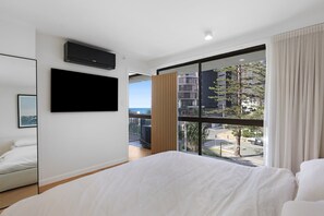 A modern hotel room with a large bed, a flat-screen TV, a balcony with a view of the city, and a window with curtains. - Longbeach 204 - 1 Bedroom Superior (Surfers Paradise)