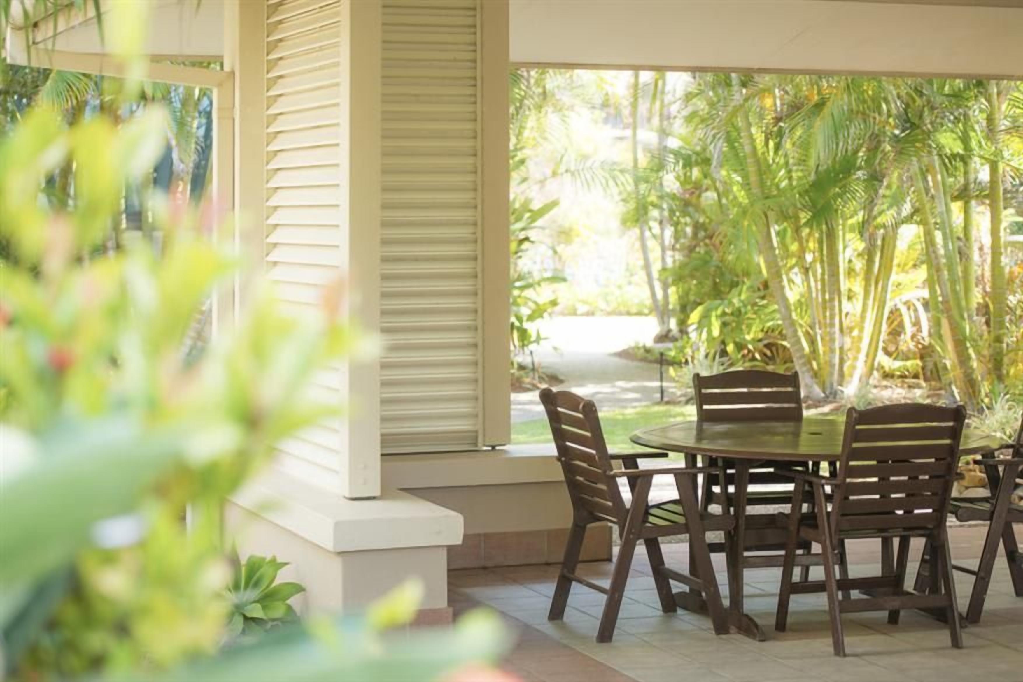 Un espace de restauration en plein air avec une table ronde et des chaises, entouré d’une végétation luxuriante.