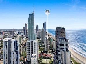 A coastal cityscape with high-rise buildings, including a prominent skyscraper, and a clear view of the ocean. - Longbeach 204 - 1 Bedroom Superior (Surfers Paradise)