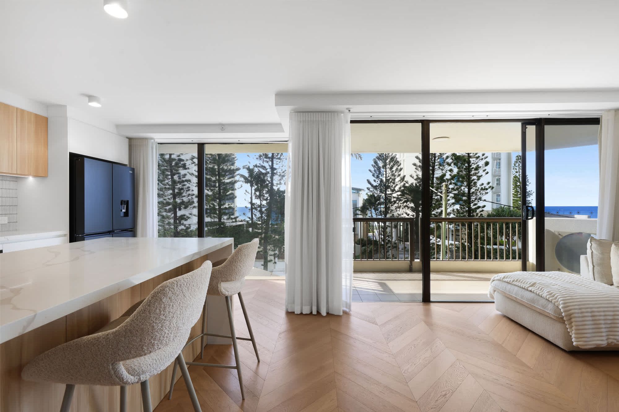 A modern apartment with a kitchen, bar area, and a balcony with a view of trees and buildings.