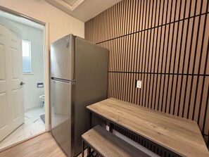 Uma cozinha compacta com geladeira embutida, um banco de madeira e painel de parede em madeira vertical.
