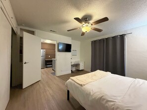 Ein Hotelzimmer mit Bett, Schreibtisch, Fernseher, Deckenventilator und einem durchgegangenen Tür sichtbaren Badezimmer.