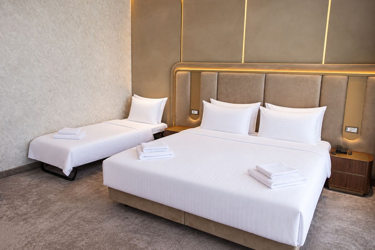 A hotel room with two single beds and one double bed, all with white linens and pillows.