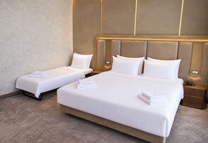 Een hotelkamer met twee eenpersoonsbedden en een tweepersoonsbed, allemaal voorzien van witte lakens en kussens.