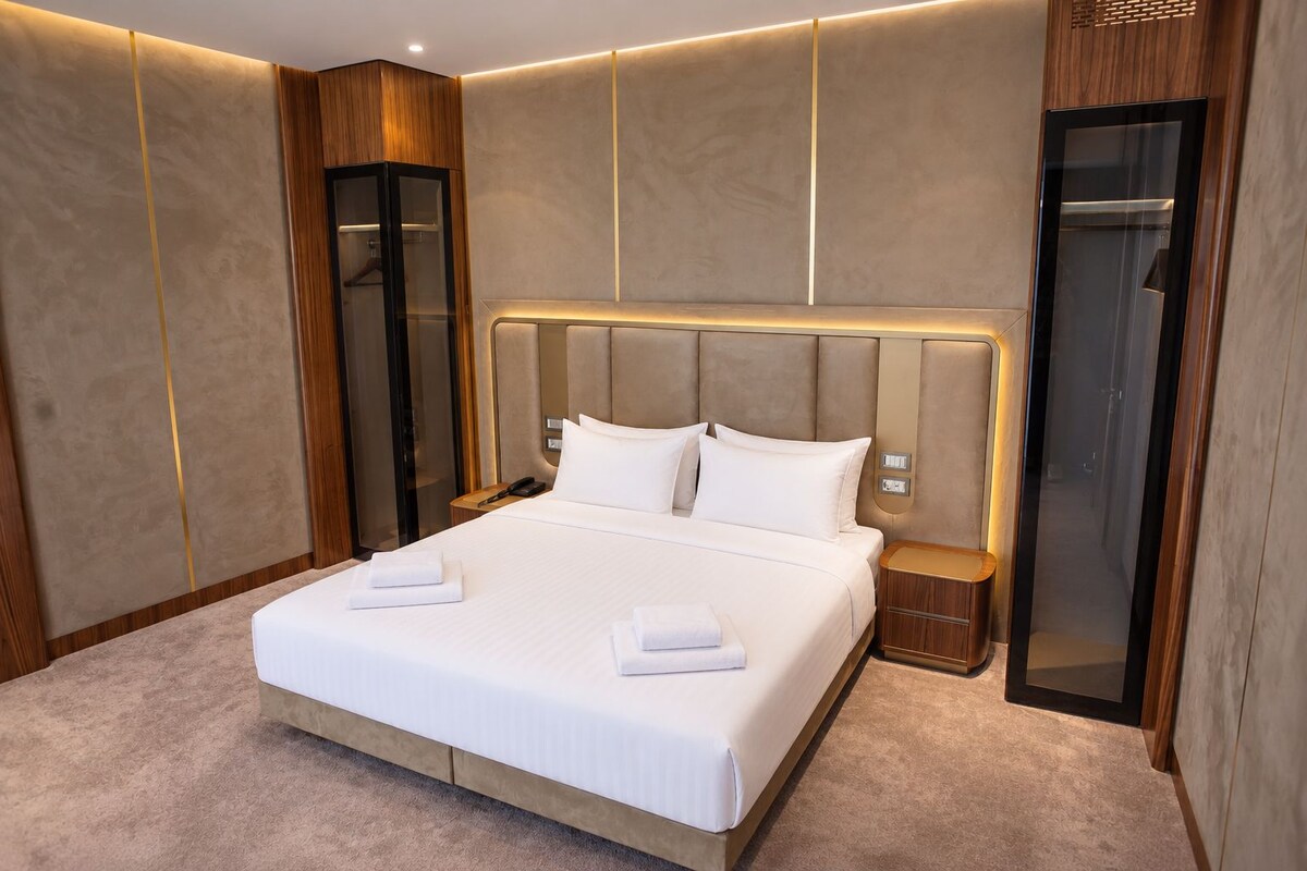 A modern hotel room with a large bed, bedside tables, a wardrobe, and a mirror.