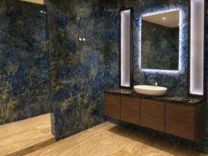 A bathroom with a marble wall, a sink, and a mirror.