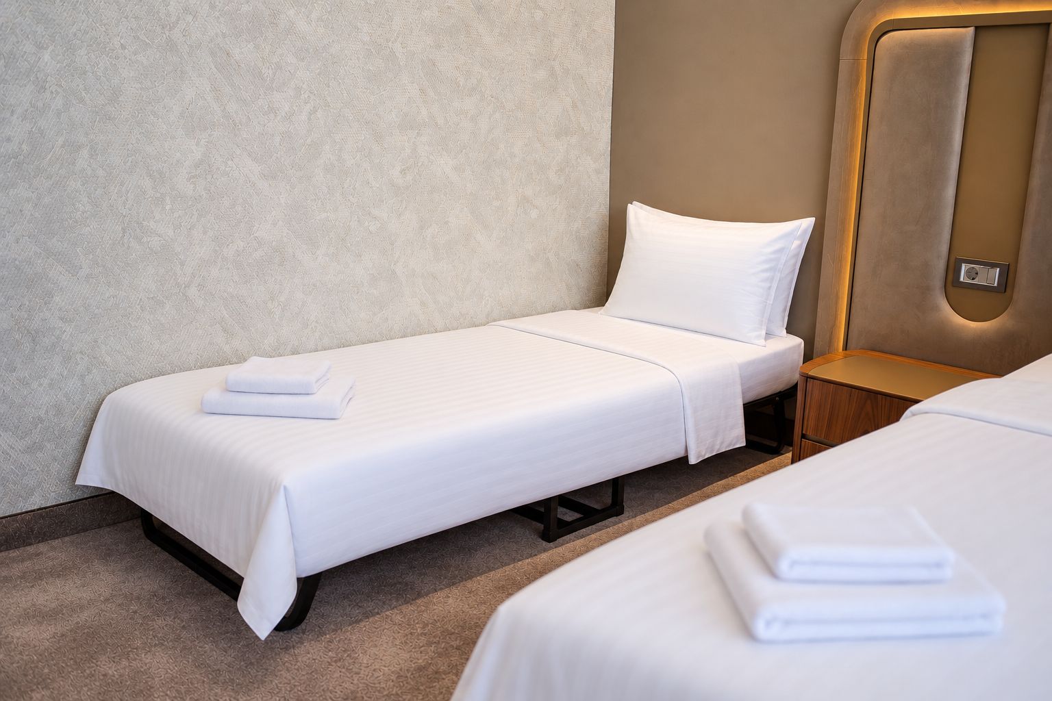 Habitación de hotel con una cama individual, una mesita de noche y un panel de control en la pared.