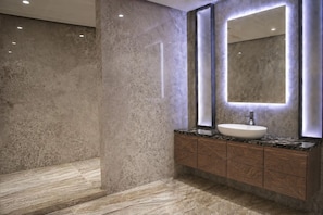 Un baño moderno con piso de mármol, un espejo grande con iluminación integrada y un tocador de madera con lavamanos.