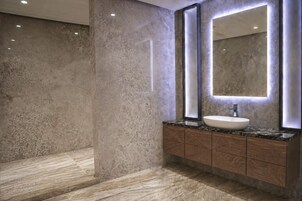 Een moderne badkamer met een marmeren vloer, een grote spiegel met ingebouwde verlichting en een houten wastafelmeubel met een wastafel.
