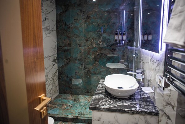 A bathroom with a large white sink, a glass shower enclosure, and a marble-tiled floor.