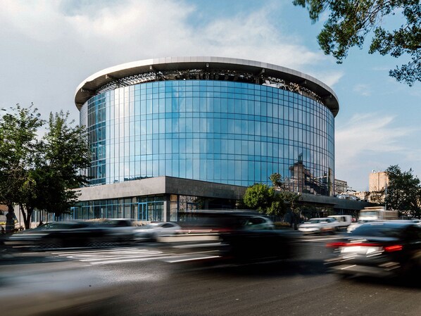 A modern building with a curved glass facade, surrounded by a busy street with moving vehicles. - The Arte Hotel (Yerevan)
