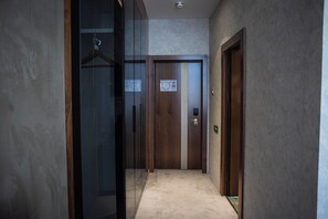 A narrow hallway with a wooden door at the end, a coat rack to the left, and a carpeted floor.