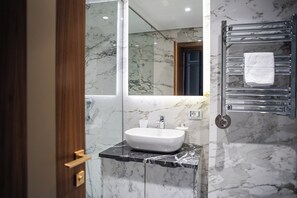 A modern bathroom with a marble sink, a mirror, and a towel rack.