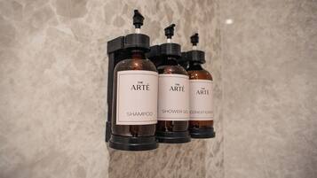 Tres botellas de productos de la marca Arté: champú, gel de ducha y acondicionador, sujetas a una pared.
