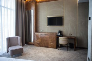 A hotel room with a large bed, a seating area with a chair, a desk with a television, and a coffee maker.