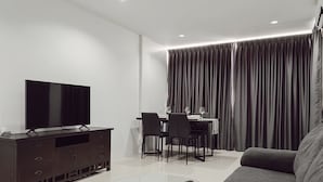 Una sala moderna con televisor de pantalla plana, muebles de madera oscura, una mesa de centro de vidrio y una zona de comedor con mesa y sillas.