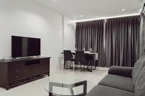 Una sala moderna con televisor de pantalla plana, muebles de madera oscura, una mesa de centro de vidrio y una zona de comedor con mesa y sillas.