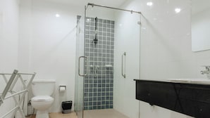 Un baño con cabina de ducha de vidrio, inodoro blanco y lavamanos negro.