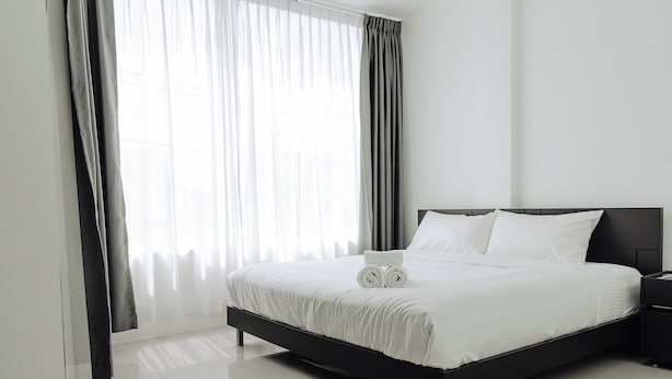 Una habitación de hotel moderna con una cama grande, ropa de cama blanca y una mesita de noche.