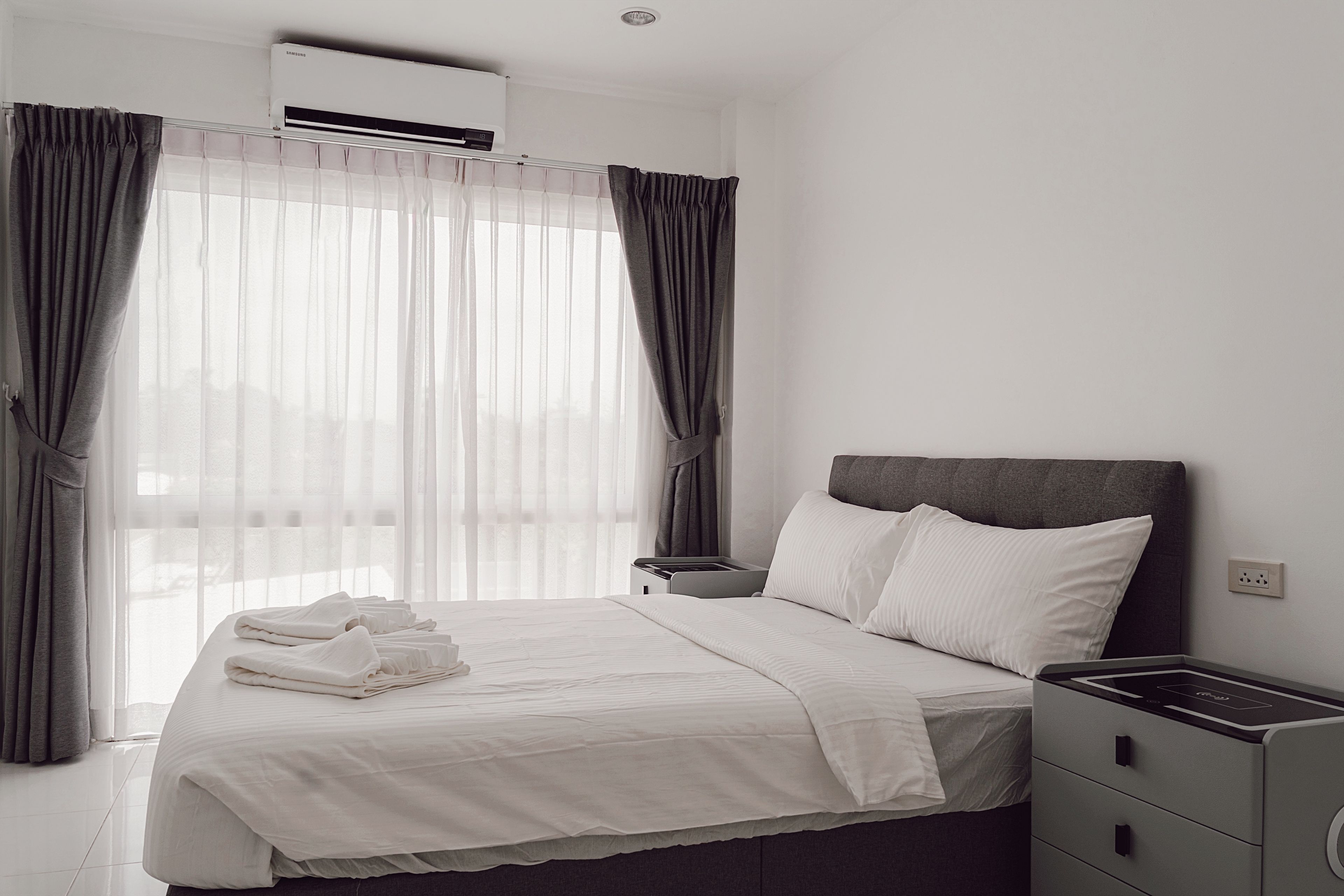 A hotel room with a bed, bedside table, and a wall-mounted air conditioner.