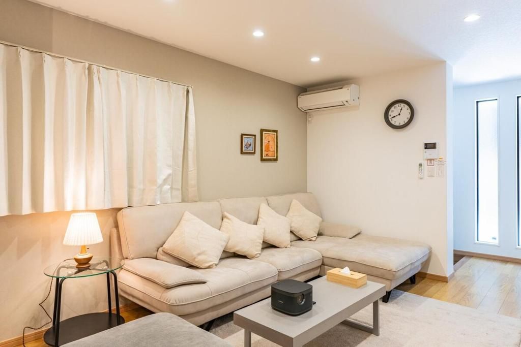 A living room with a beige sofa, a glass coffee table, a lamp, and a clock on the wall.