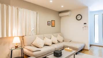 A living room with a beige sofa, a glass coffee table, a lamp, and a clock on the wall.