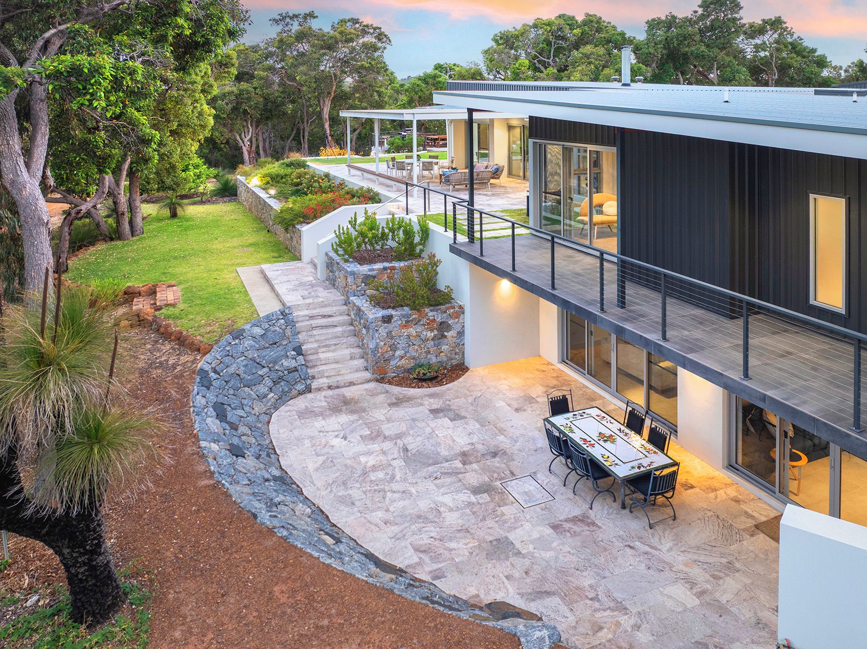 A modern house with a patio, outdoor seating, and a stone retaining wall.