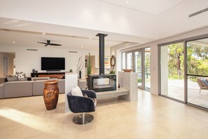 A modern living room with a fireplace, a sofa, a television, and a large window. - Amira Vista - Views of Eagle Bay (Eagle Bay)