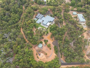 An aerial view of a property with a large building, multiple green-roofed structures, and a dirt road. - Amira Vista - Views of Eagle Bay (Eagle Bay)