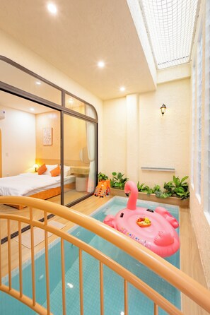 A hotel room with a bed, a window, a small pool with a pink flamingo float, and a safety rail. - Nimi Han River: 3BR-4 Beds | Private Pool & Beach (Đà Nẵng)