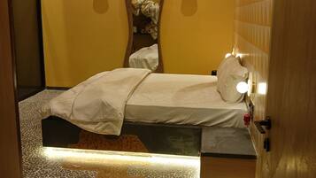 A room with a bed, a mirror, a wall-mounted light fixture, and a patterned floor.