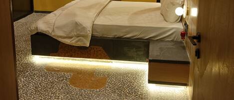 A room with a bed, a mirror, a wall-mounted light fixture, and a patterned floor.