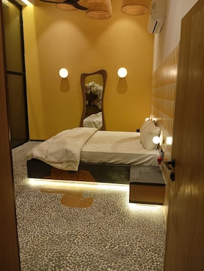Una habitación con una cama, un espejo, una lámpara en la pared y un suelo estampado.