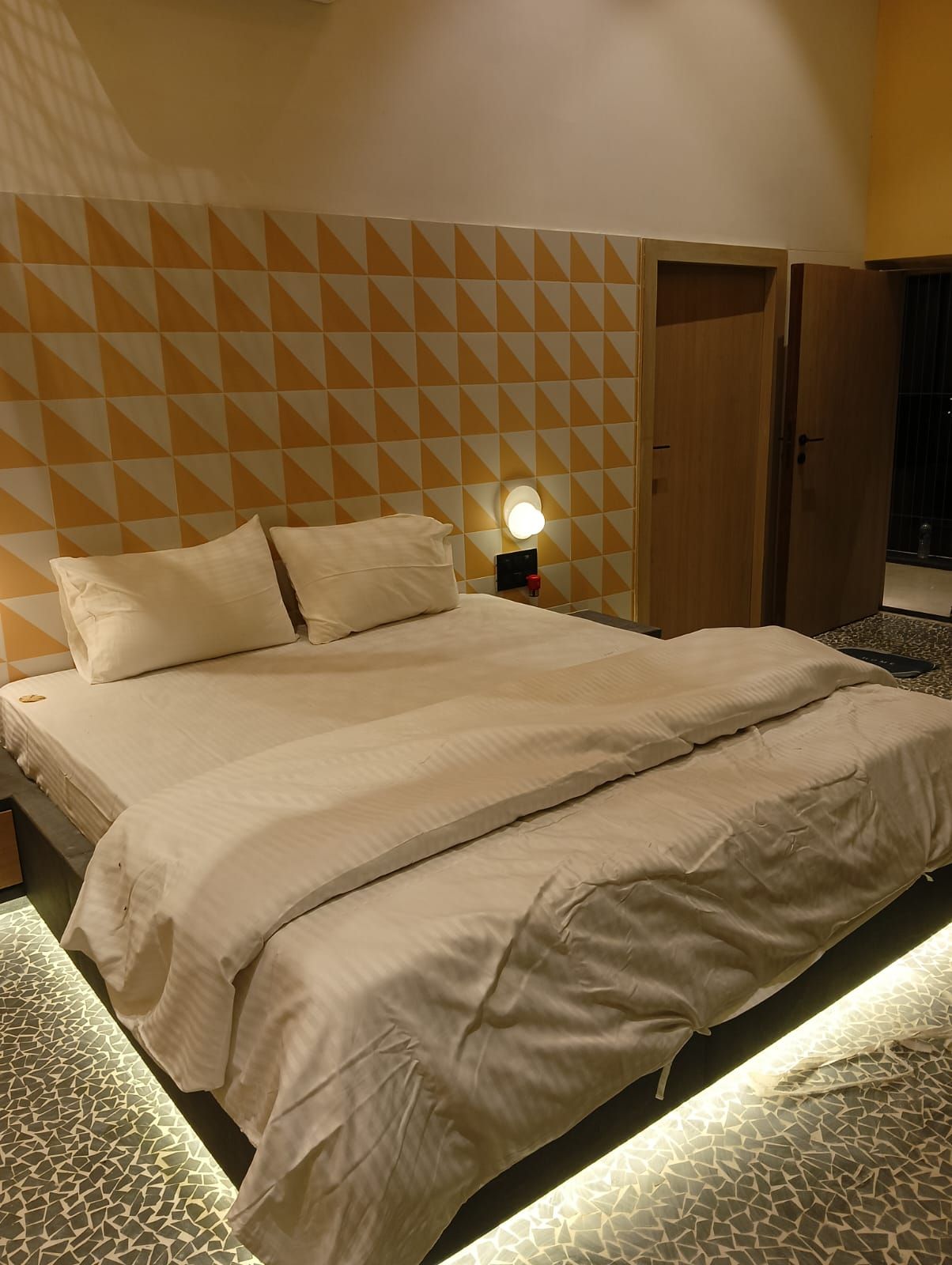Hotellihuone, jossa on sänky, yöpöytä lampun kanssa ja vaatekaappi.