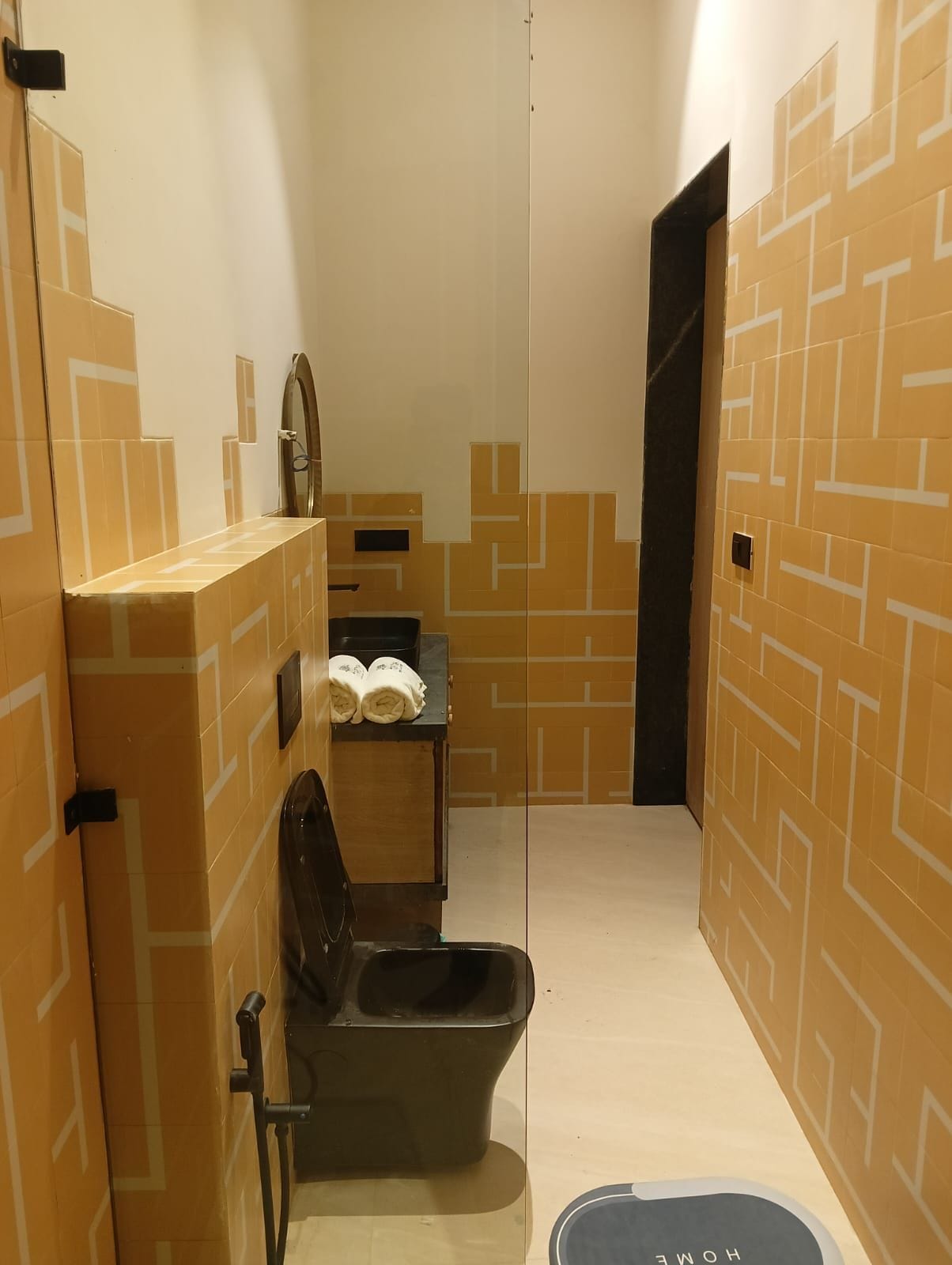A narrow bathroom with a black toilet, a small shelf with towels, and a mirror.