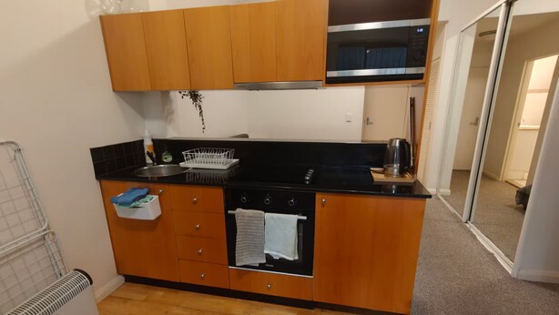 Cocina compacta con armarios de madera, encimera negra, microondas y horno empotrado.