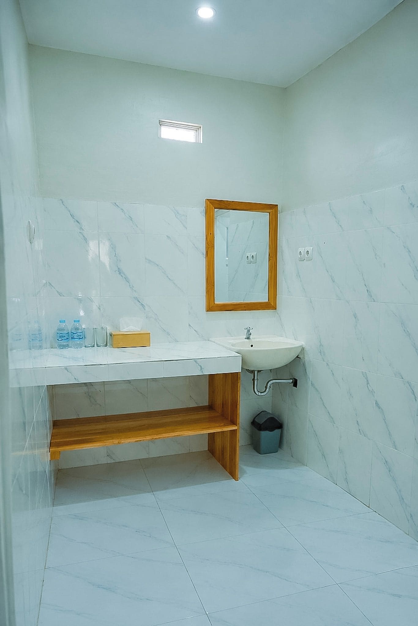 Un baño con pared de mármol, tocador de madera, lavabo y espejo.