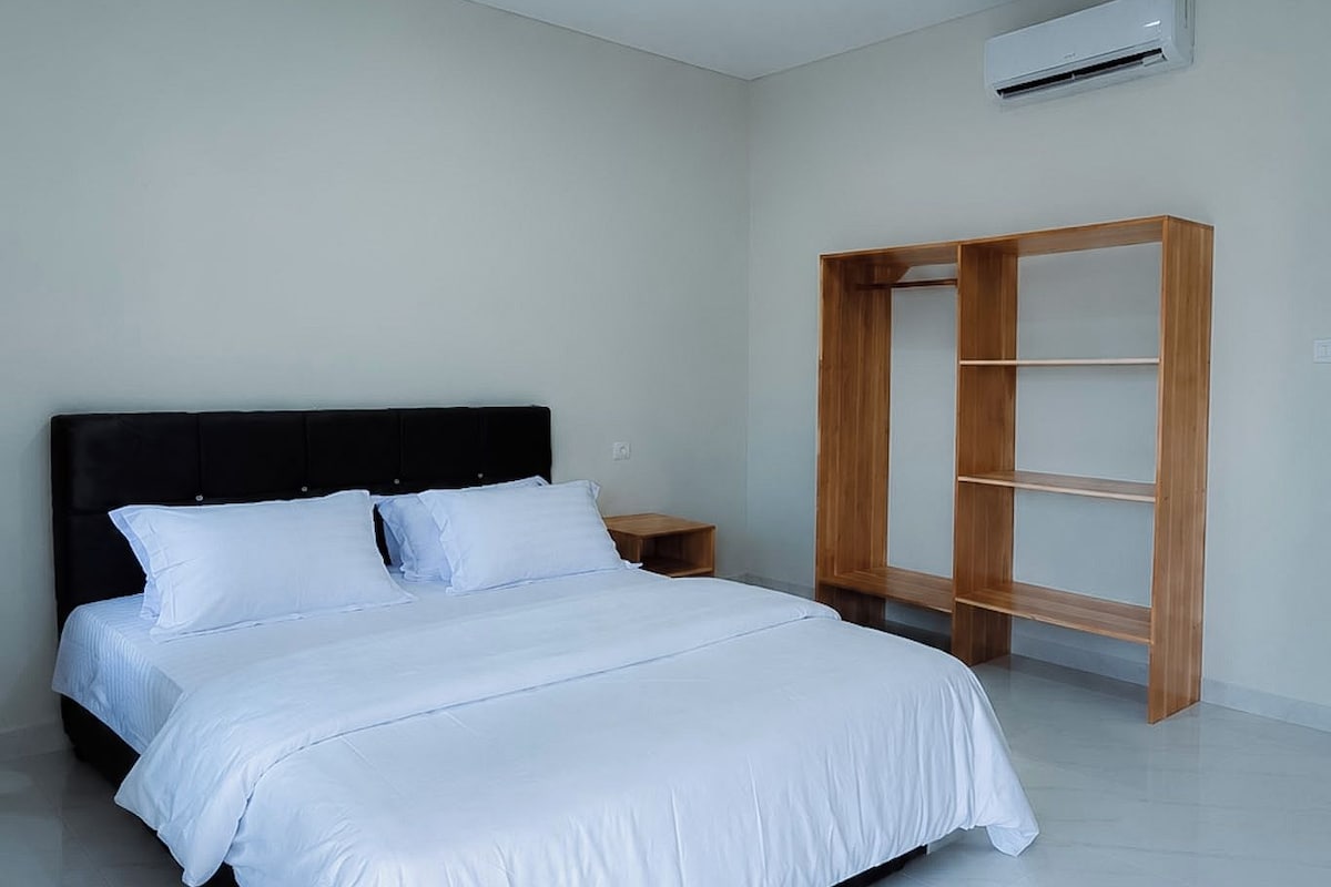 A bedroom with a bed, a nightstand, a wooden wardrobe, and an air conditioning unit.