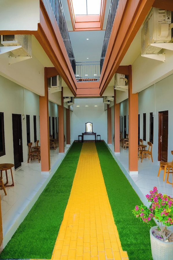 A hotel corridor with a central walkway, multiple doors, and a skylight.